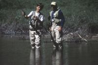 Two men are standing in the water holding fishing rods.