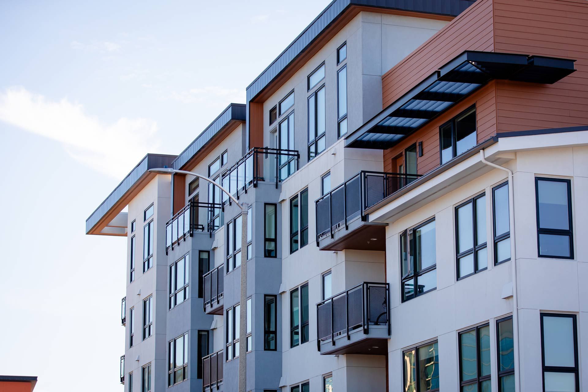 Modern apartment building with balconies, light-colored exterior, and brown accents against a blue sky.