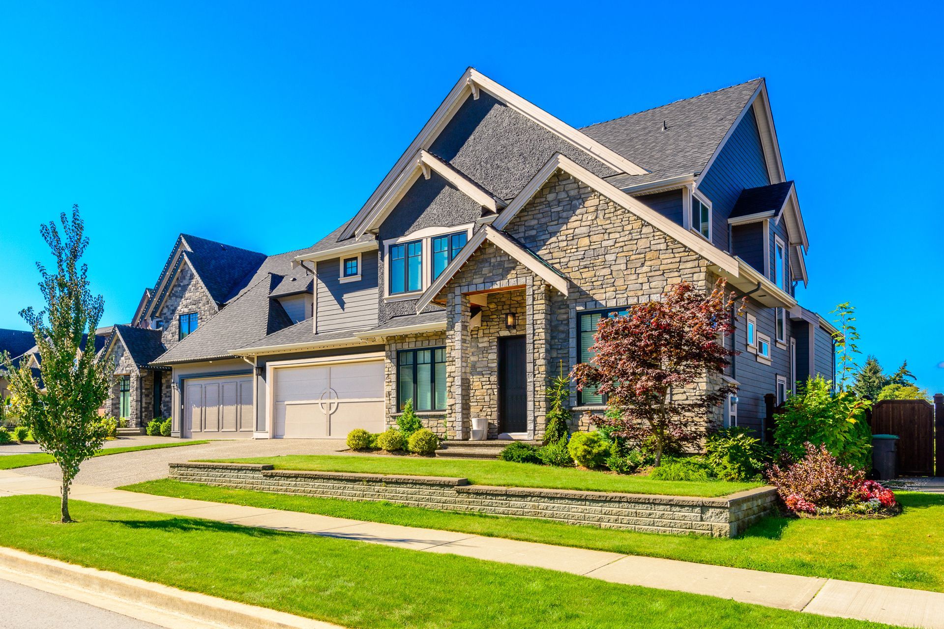 Two-story house with stone and gray siding, green lawn, and blue sky.