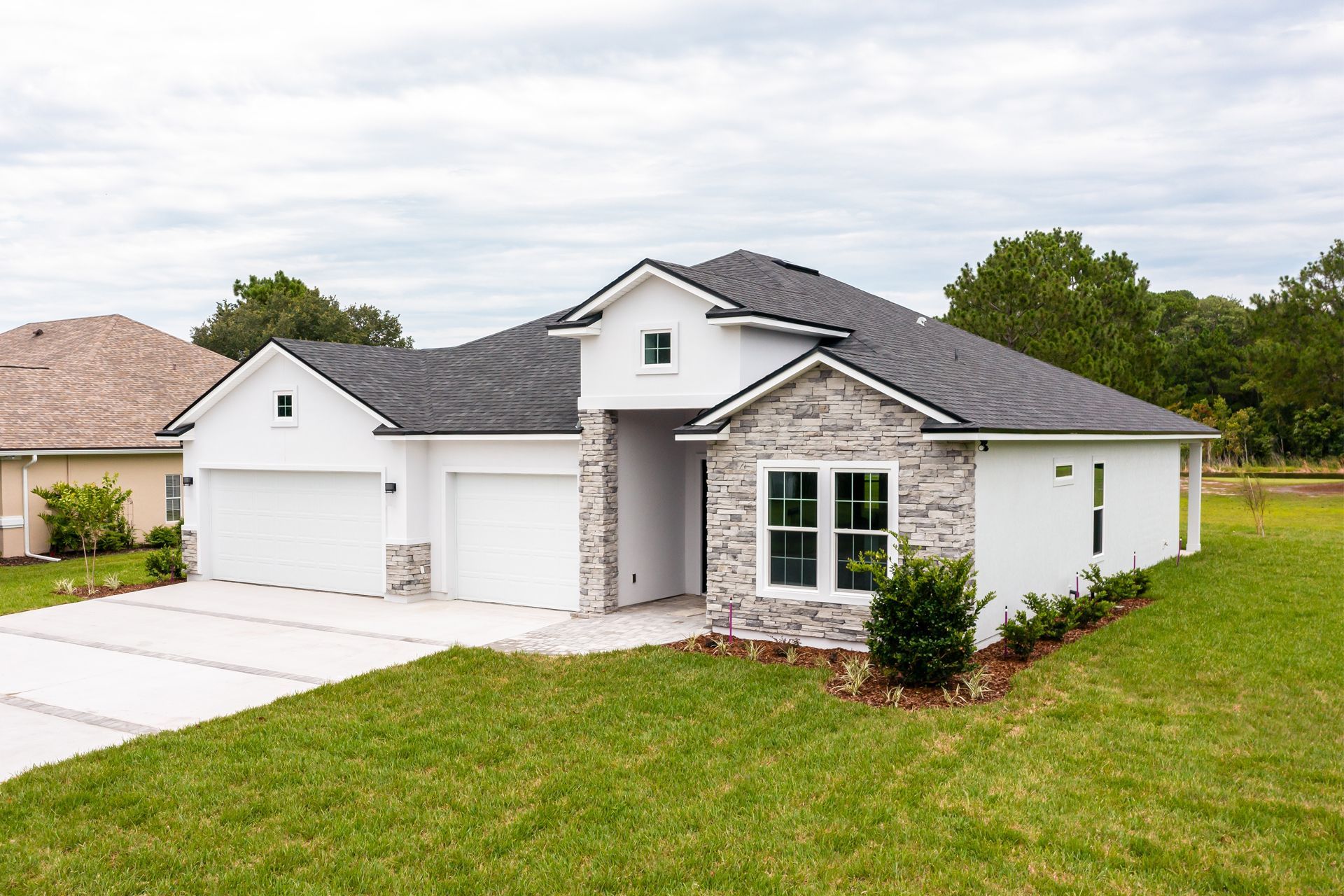 White house with stone accents, two-car garage, and green lawn on a cloudy day.