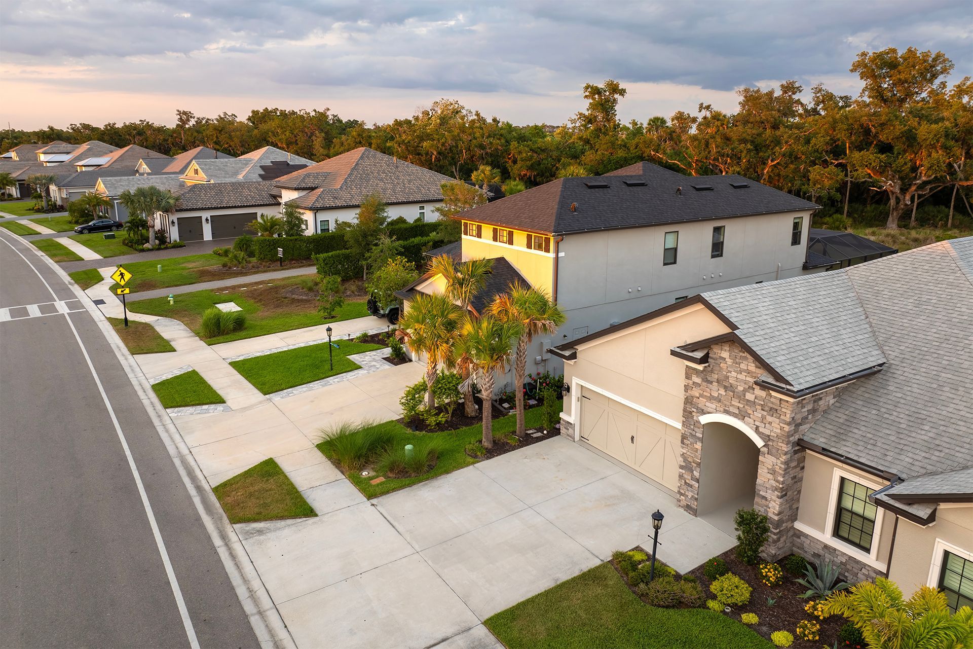 Suburban street with houses, driveways, and sidewalks at dusk, trees in the background.