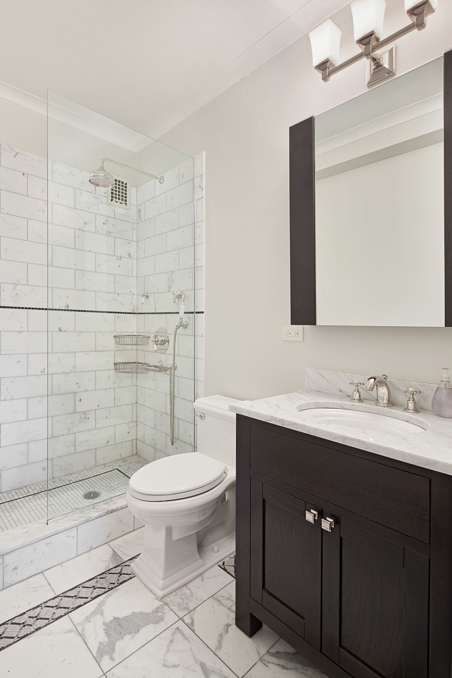 A modern bathroom featuring a white subway-tiled shower, a dark wood vanity with a white top, and marble-style flooring.