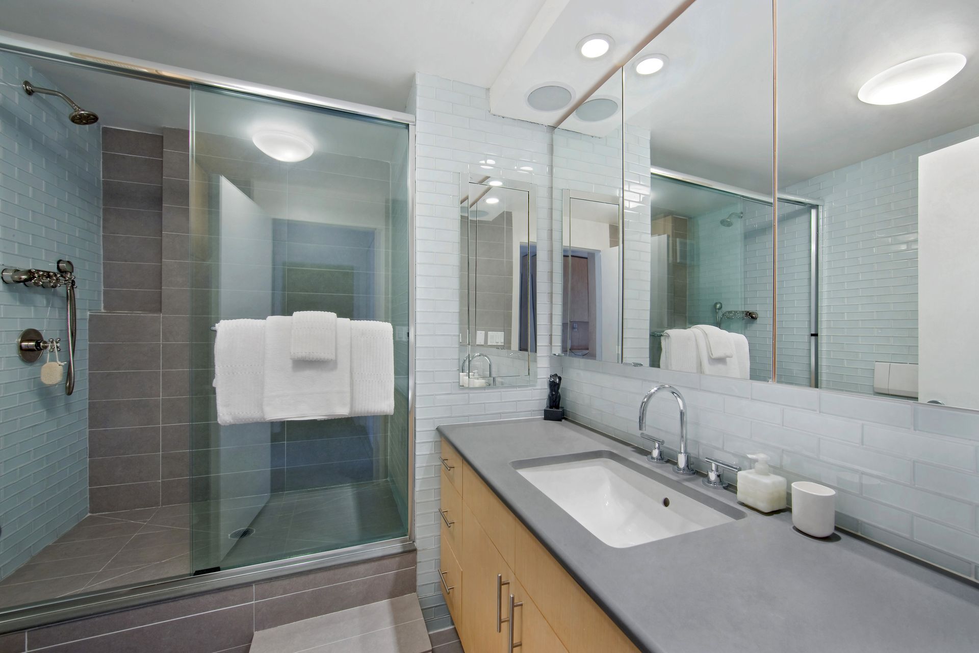 Modern bathroom featuring a glass-enclosed shower, wood vanity with grey countertop, and a large wall mirror.