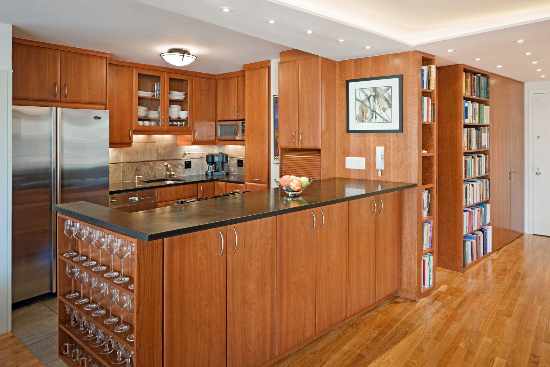 A modern kitchen features wood cabinets, a black countertop, stainless steel appliances, and built-in wine glass storage.