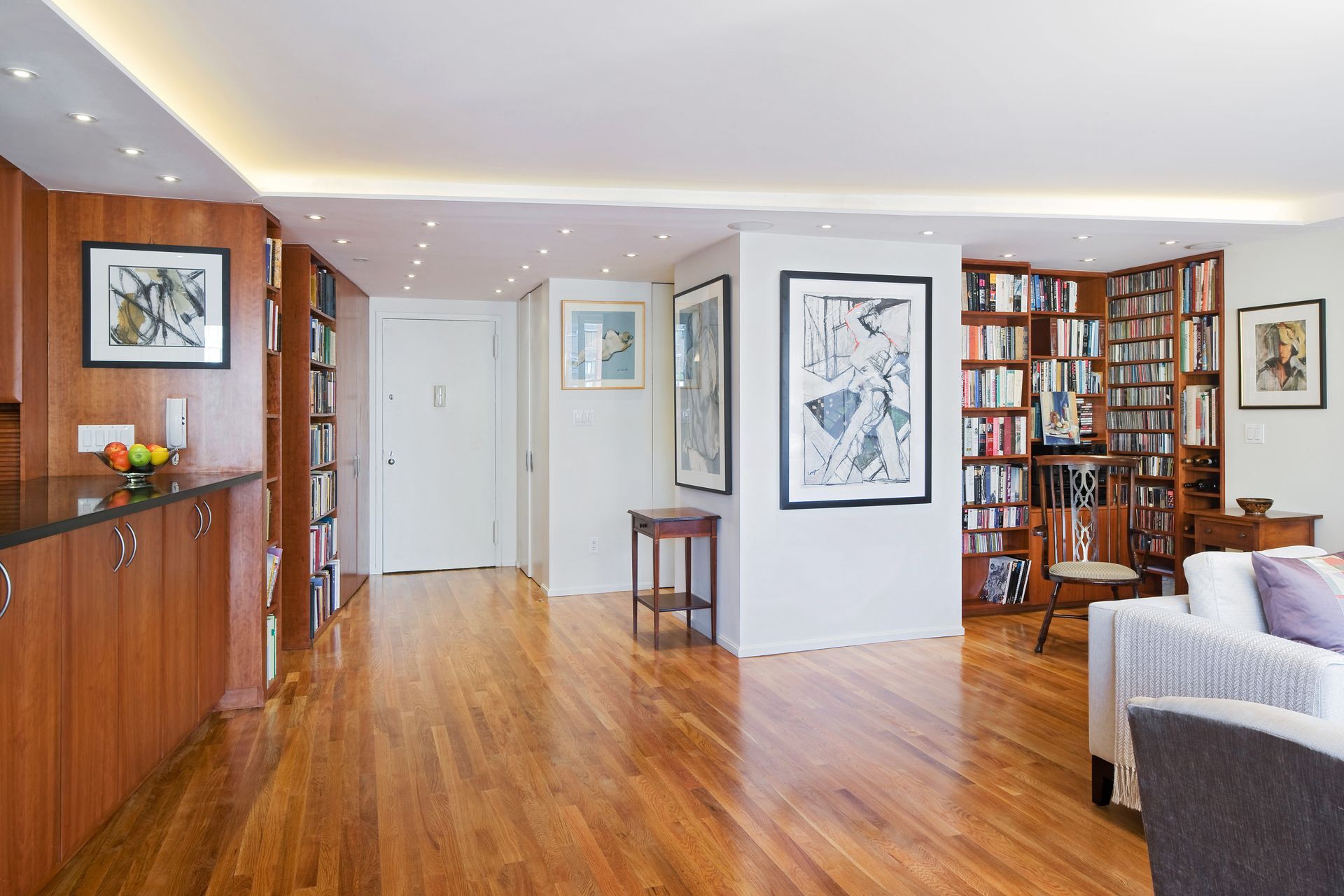 A brightly lit, modern living space features wooden floors, built-in bookshelves, framed art, and contemporary furniture.
