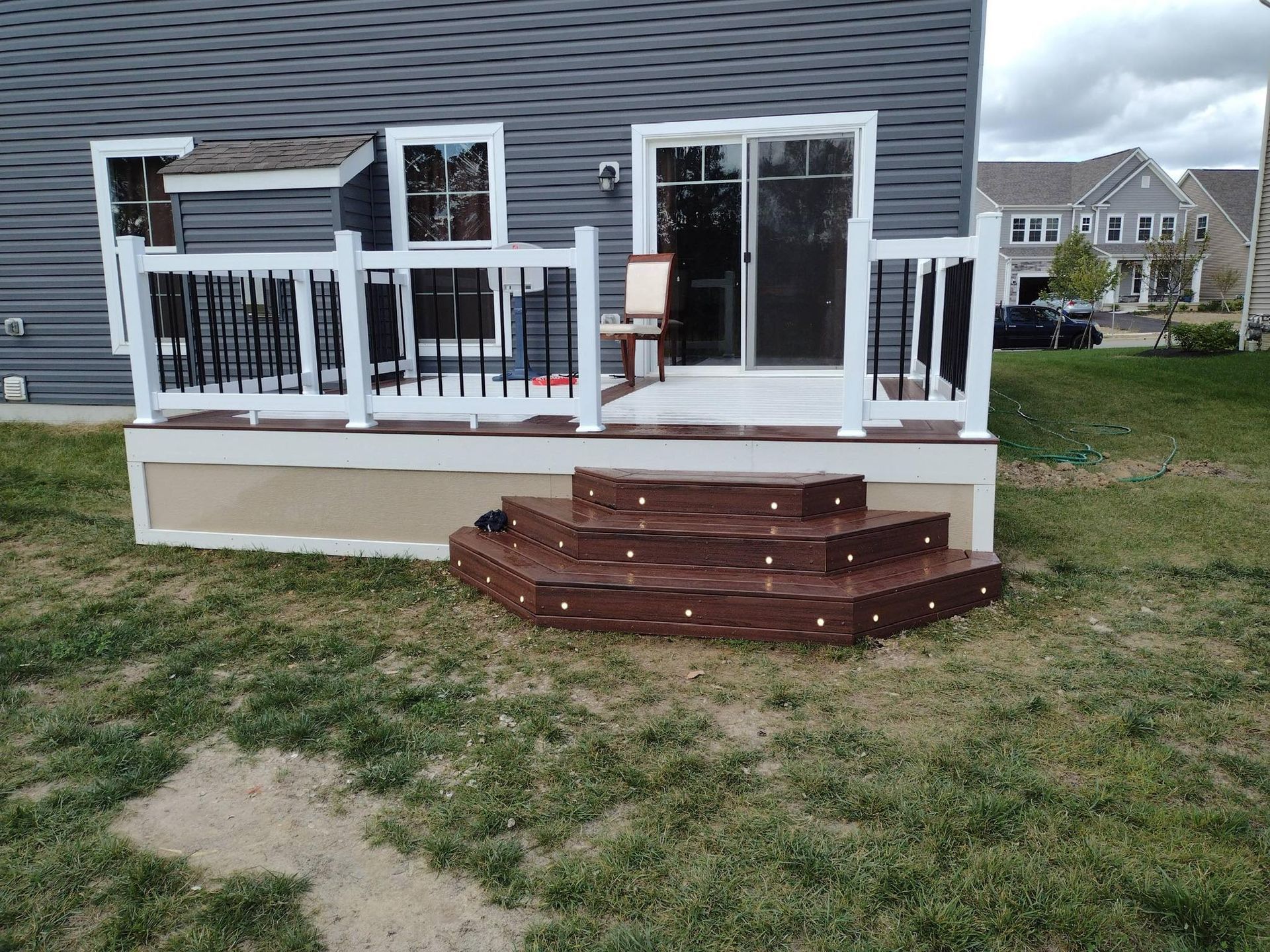 Backyard deck with dark brown steps, white railing, and a sliding glass door.