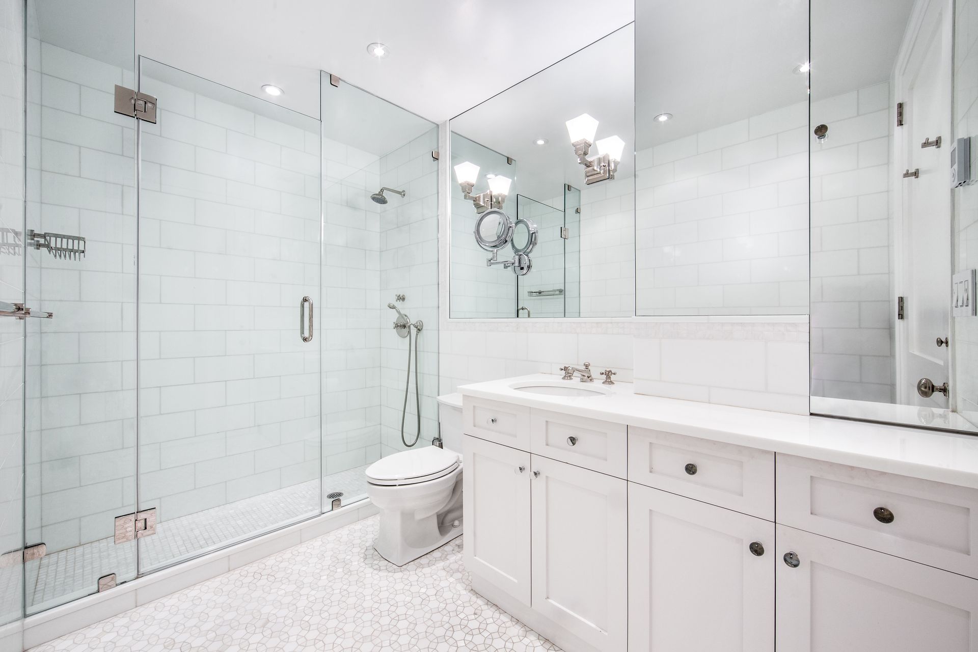 A bright, modern white bathroom featuring a glass-enclosed shower, a toilet, and a vanity with a large mirror.