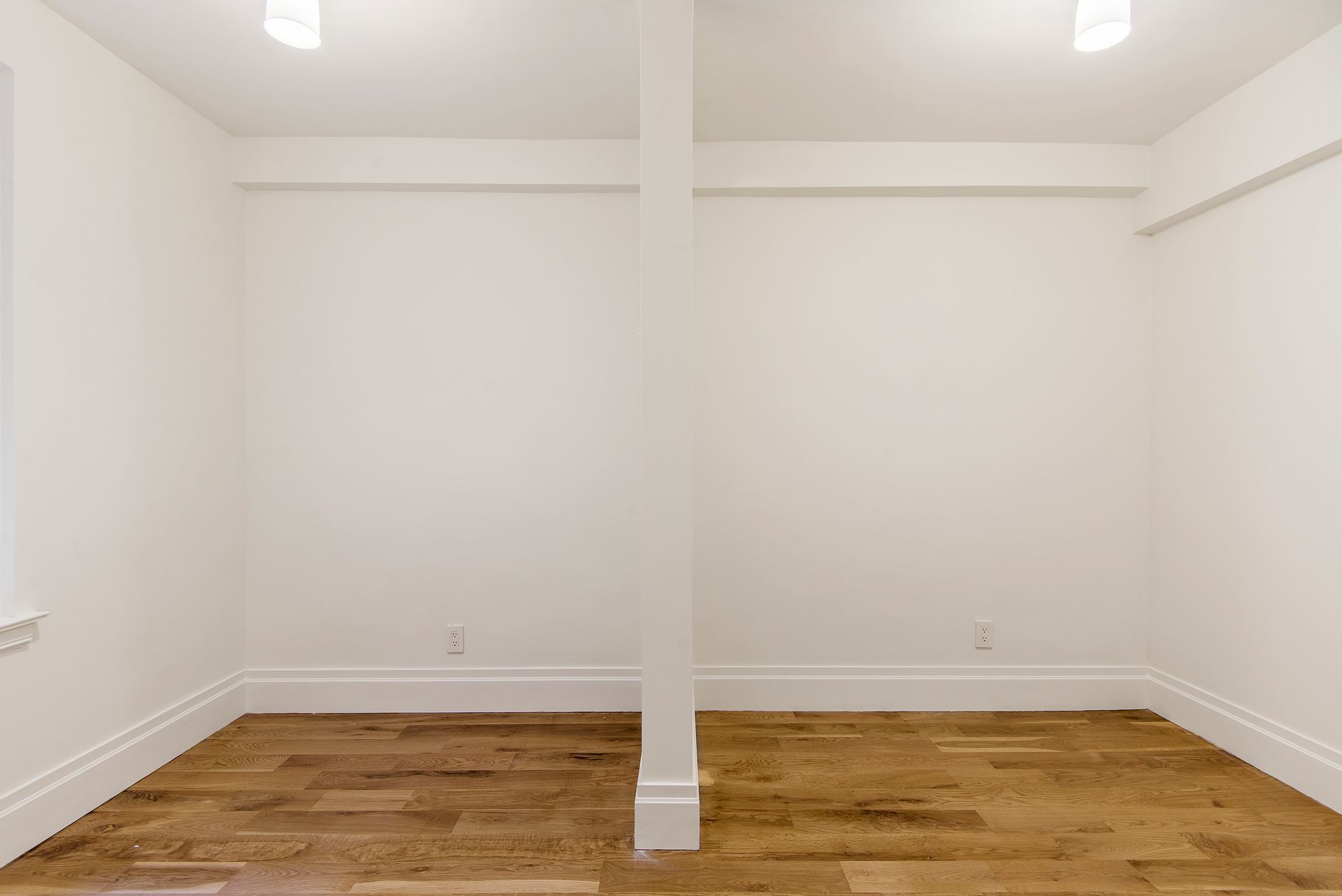 Empty room with white walls, light wood flooring, and a central structural post.