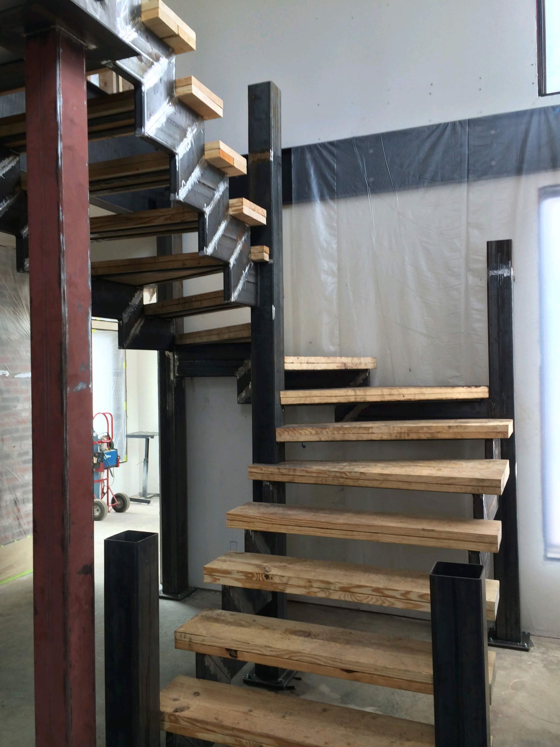 Steel and wooden staircase in a building under construction; unfinished walls, visible steel framing.