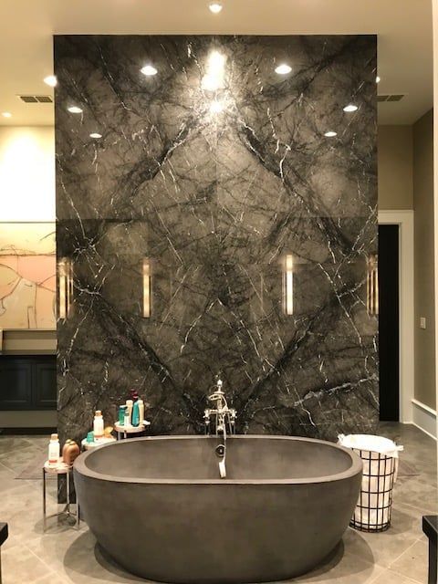 Bathroom with a dark gray marble feature wall, gray oval tub, and recessed lighting.