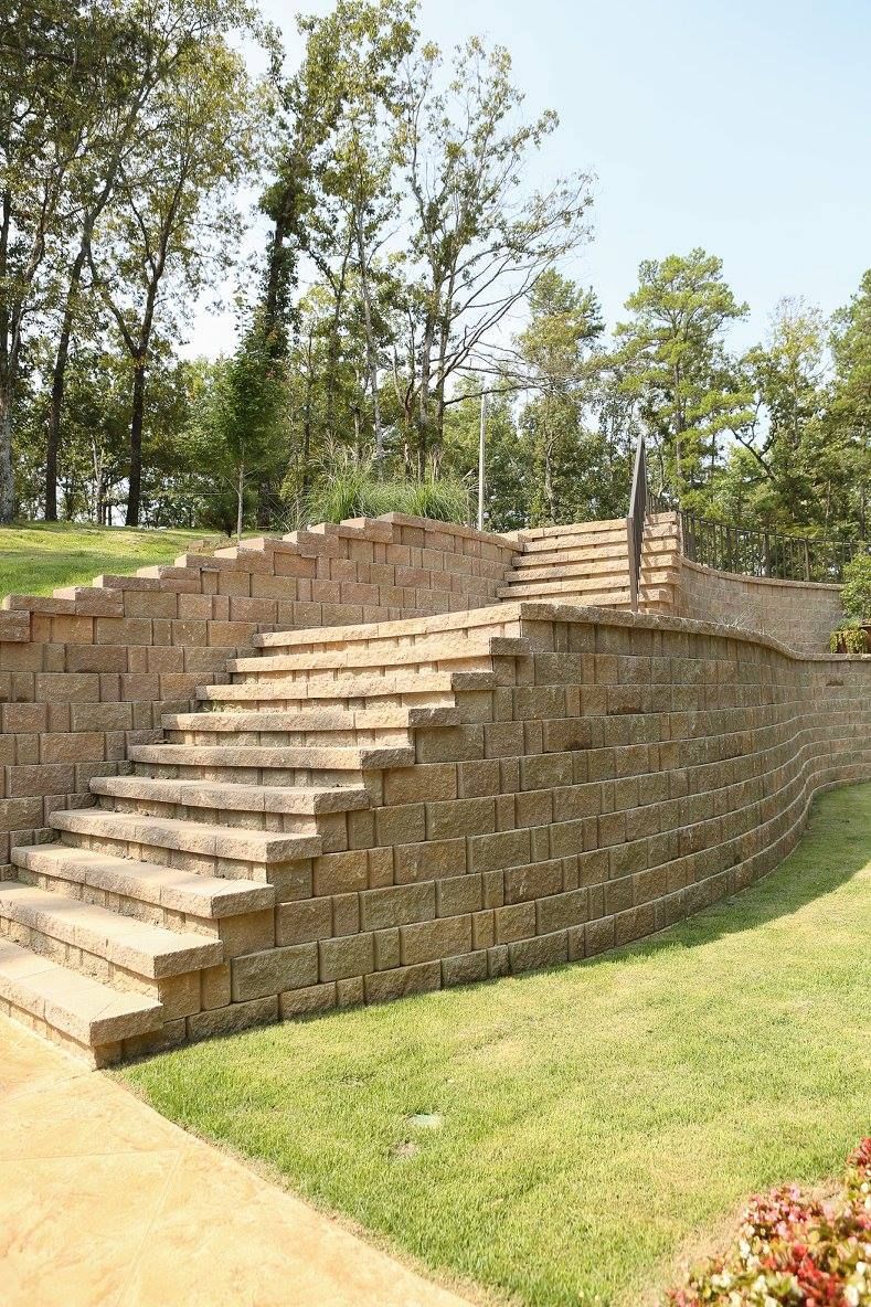 Stone stairs built into a retaining wall in a grassy yard, leading upward toward trees.