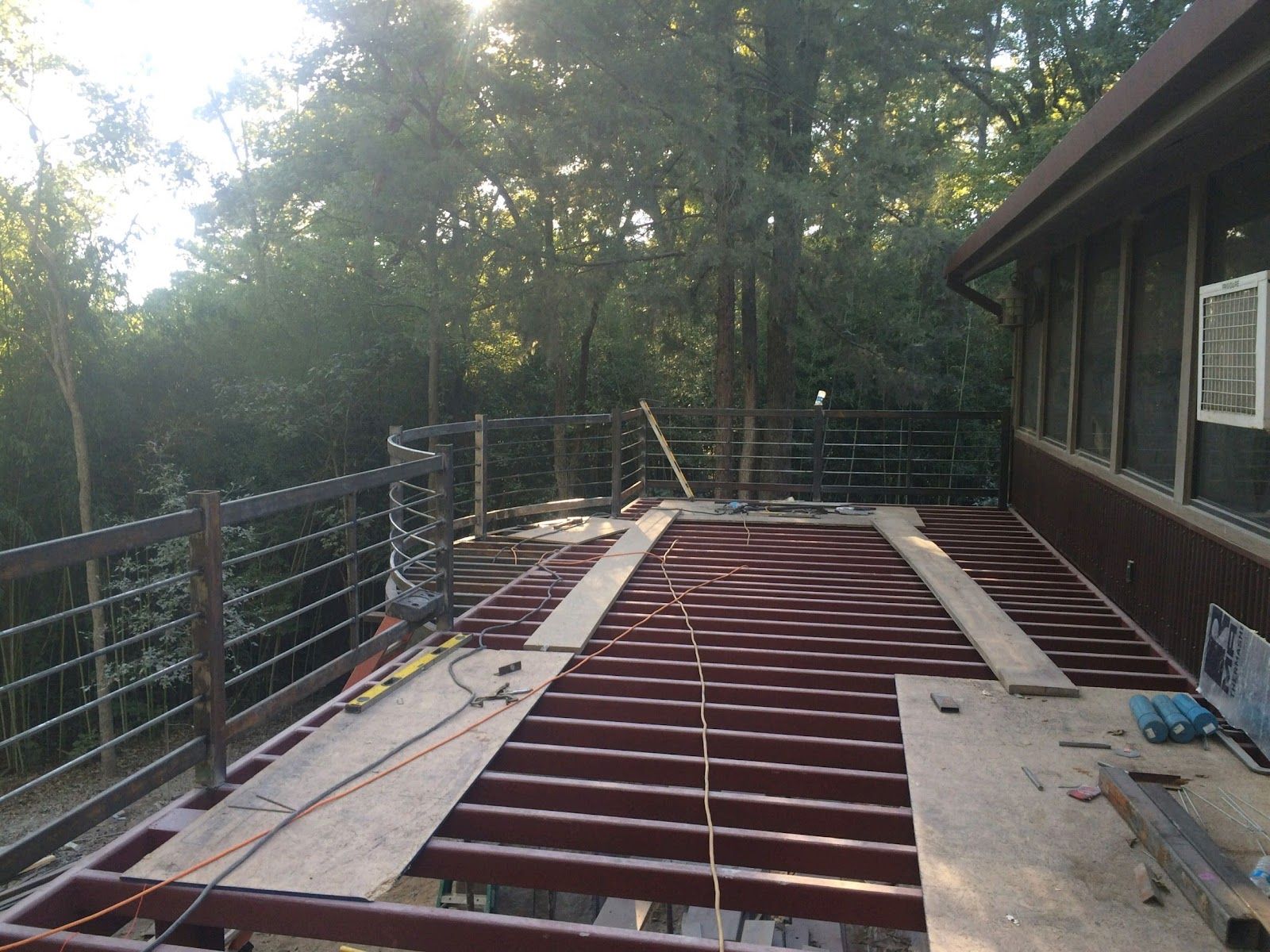 Deck under construction, overlooking trees. Metal framing with partial wood planks; brown railing.