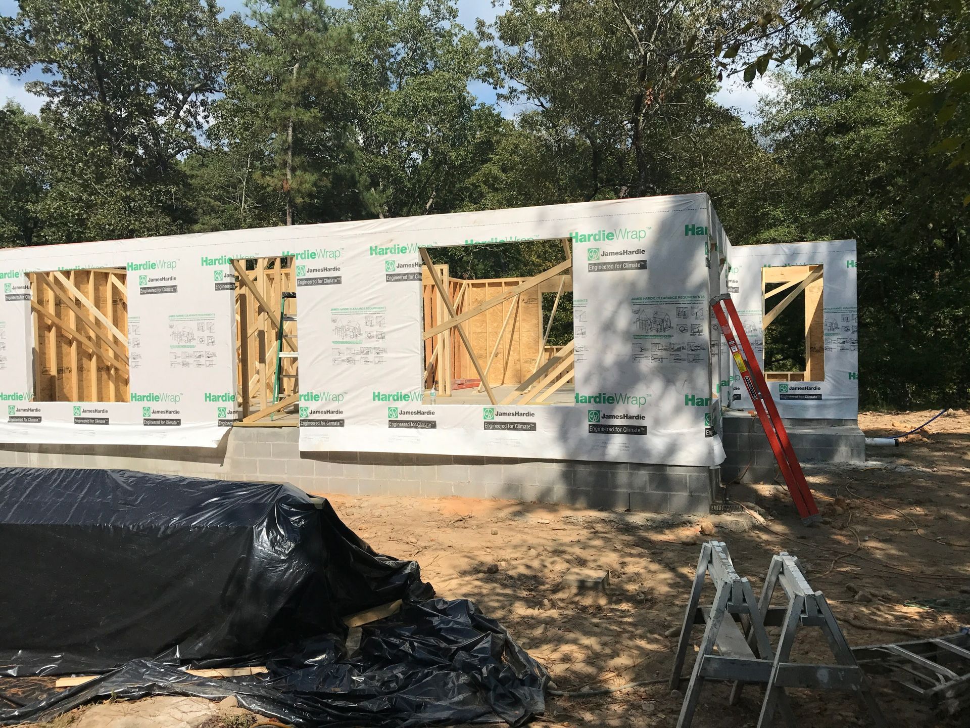 Construction of a house with wooden frame and white siding. A red ladder leans against the structure.