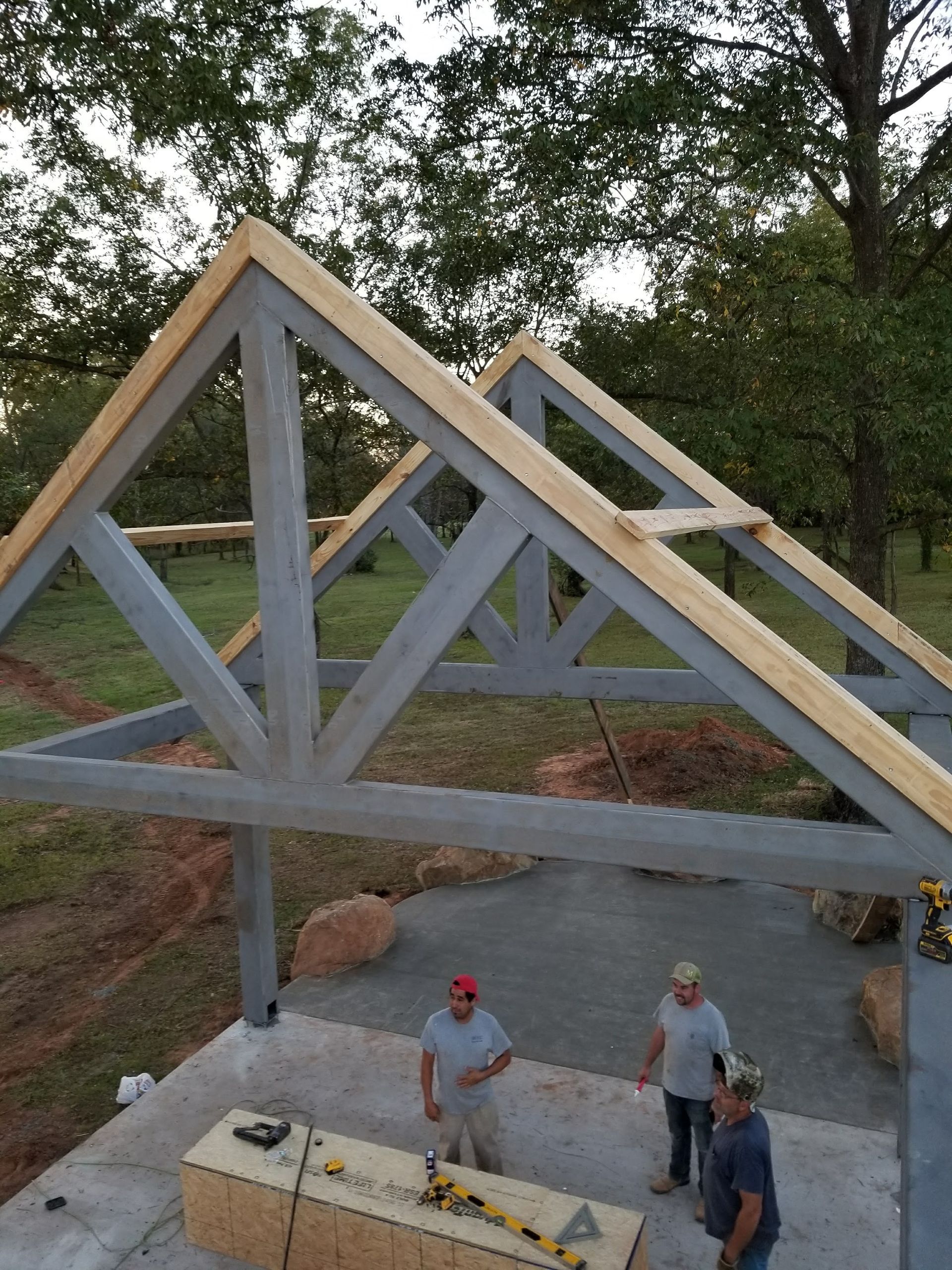 Workers building a gray and tan wooden structure outdoors. Three men stand near a table.