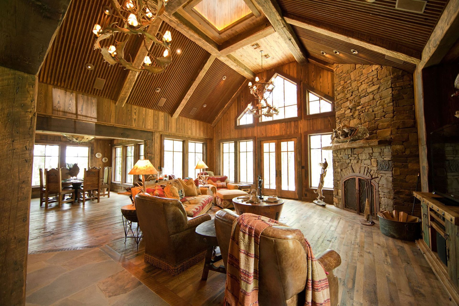 Rustic living room with high wood ceilings, stone fireplace, and large windows.