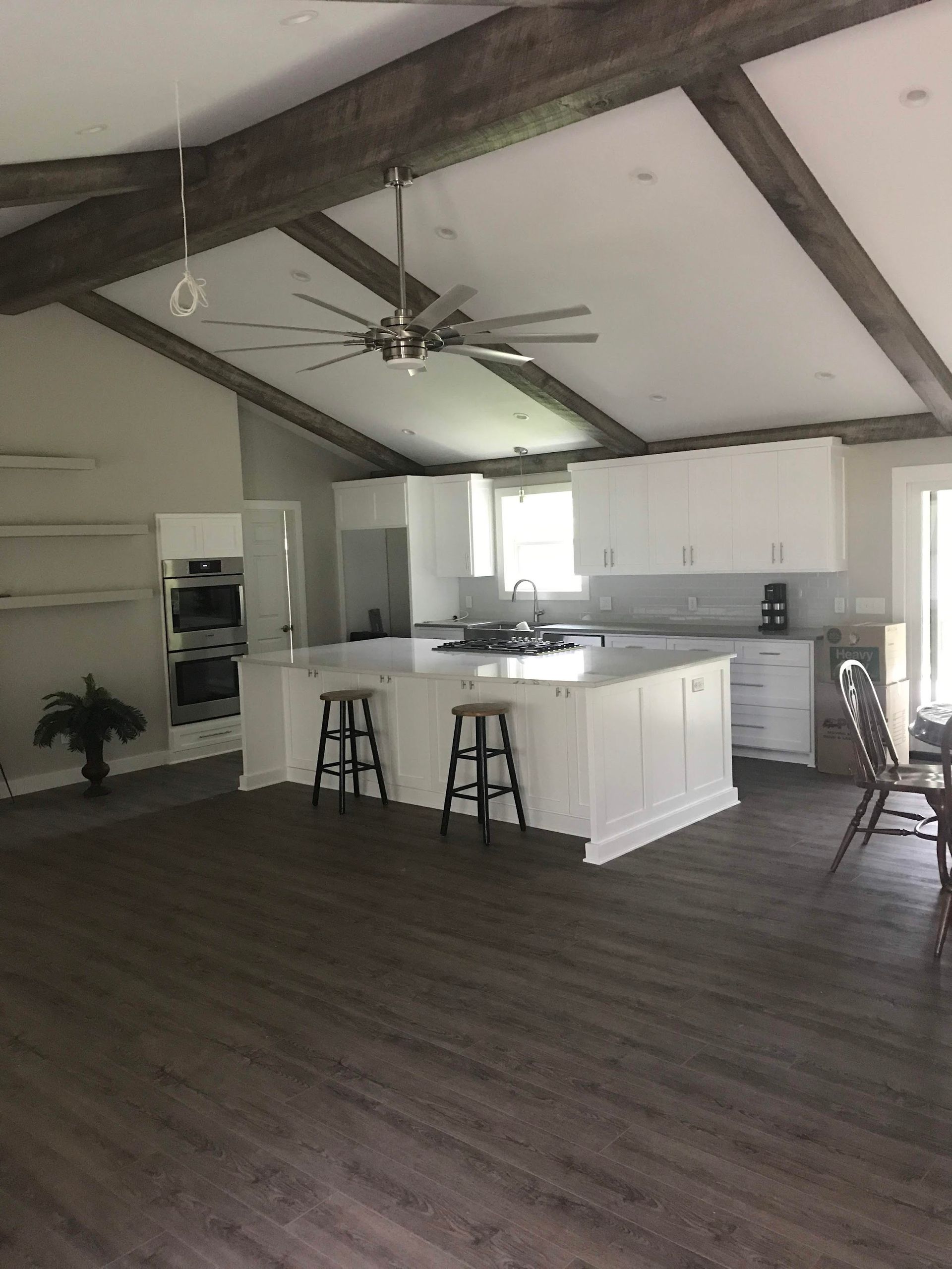 Open-concept kitchen with white cabinets, island, and ceiling beams; dark wood floors.