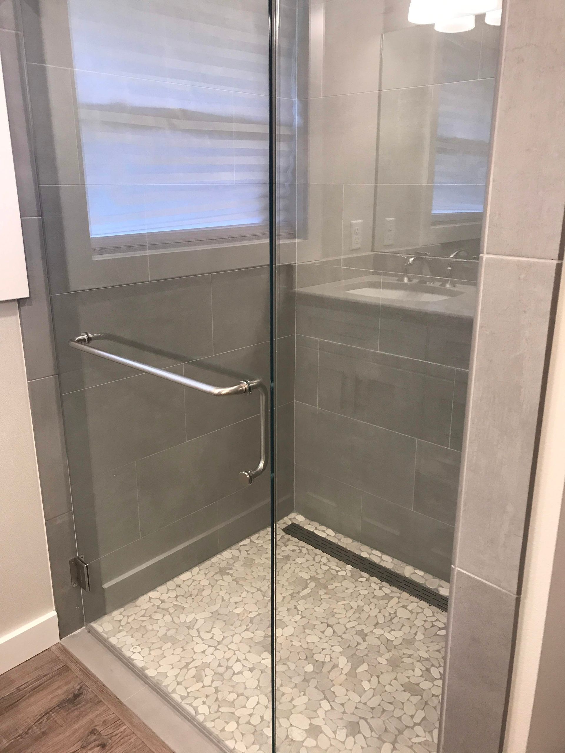 A modern walk-in shower with glass door, gray tile, and pebble floor.