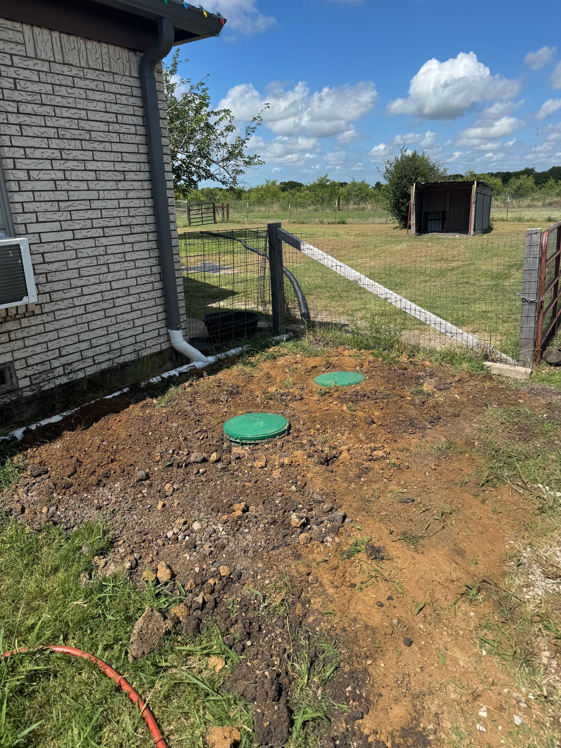 A house is sitting in the middle of a field next to a fence.