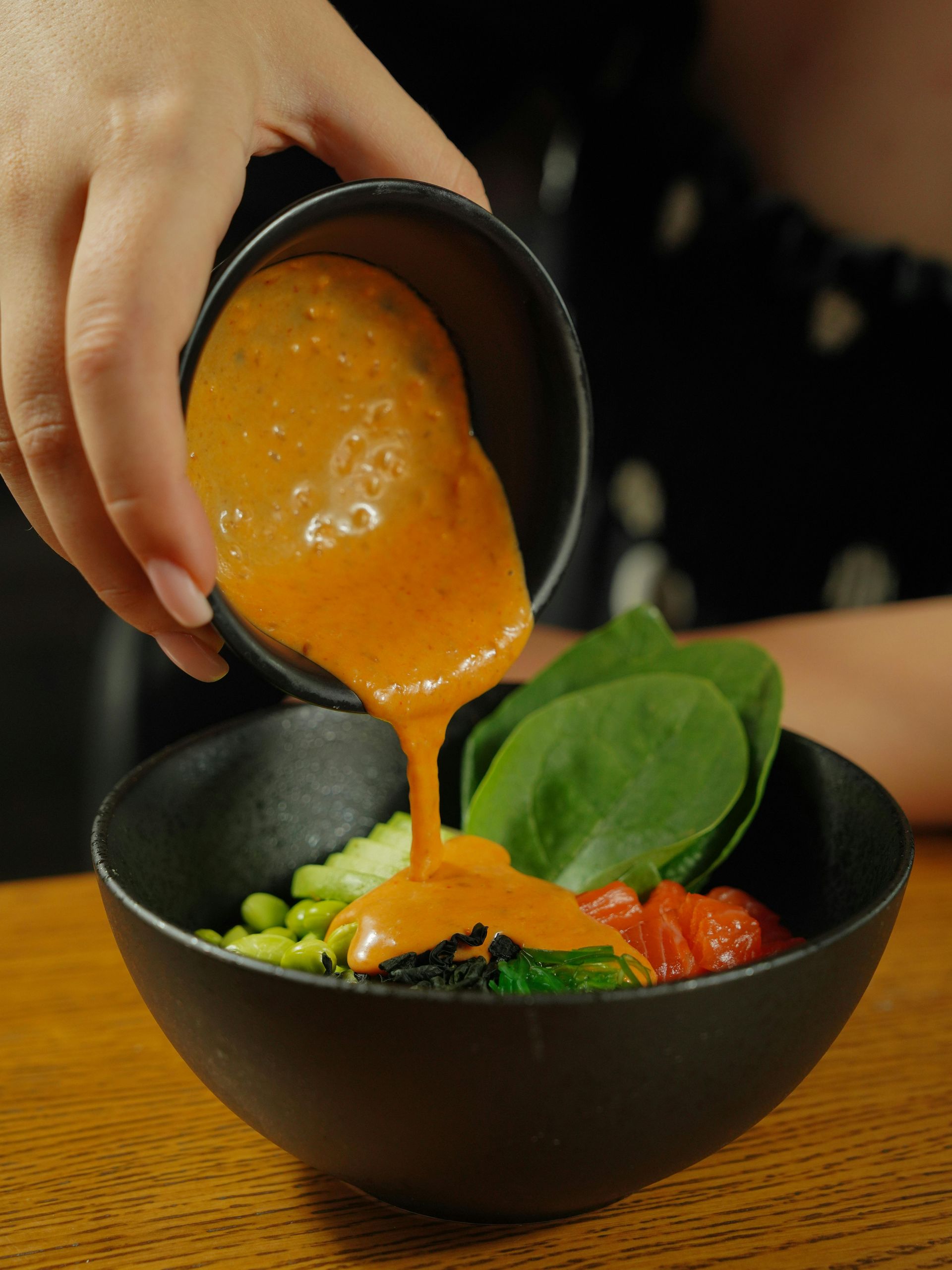Vertiendo a mano sopa de naranja en un tazón negro con guisantes, espinacas y tomates.