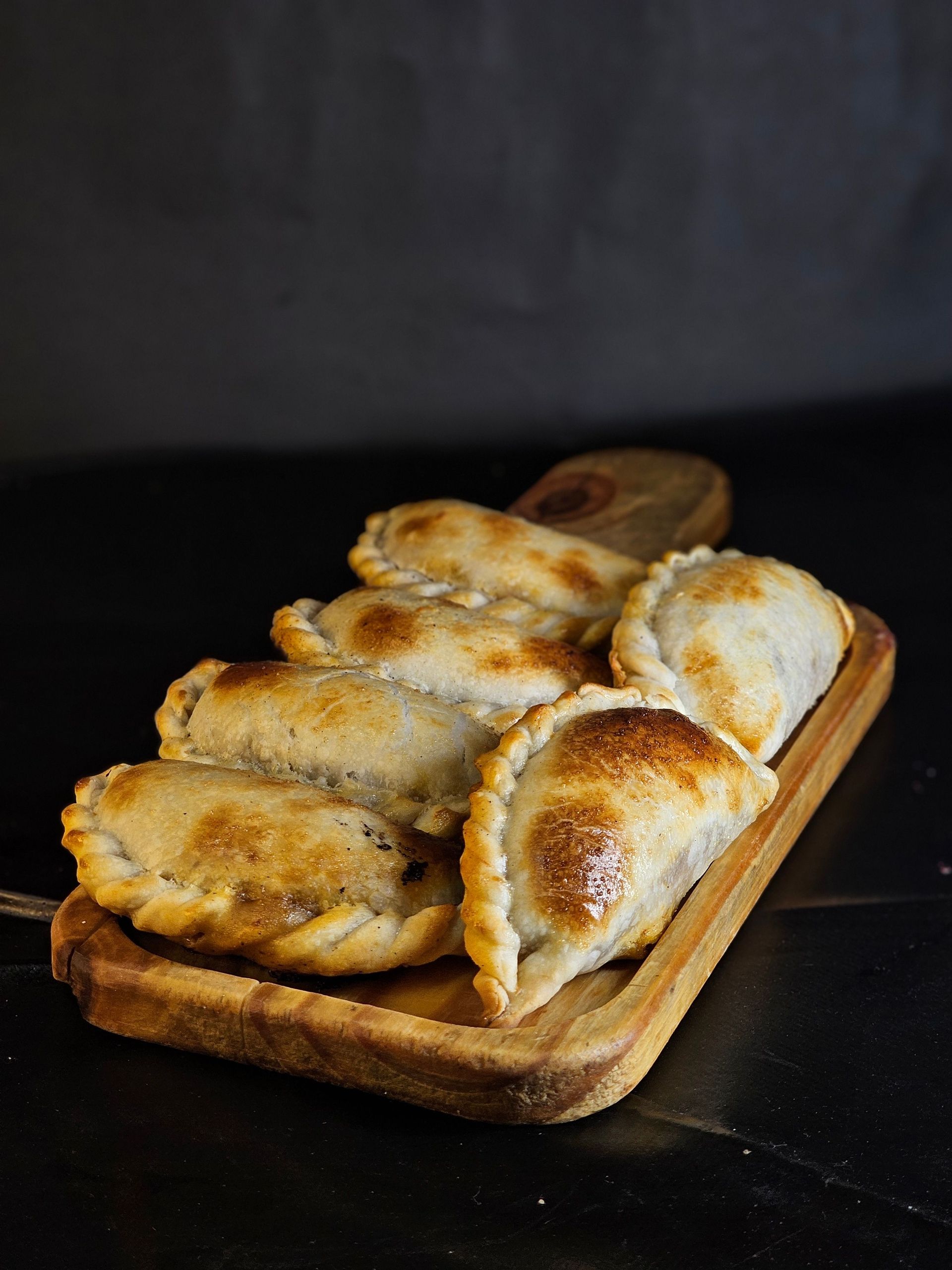 Bandeja de madera con rebanadas de pan tostado relleno sobre una mesa oscura.