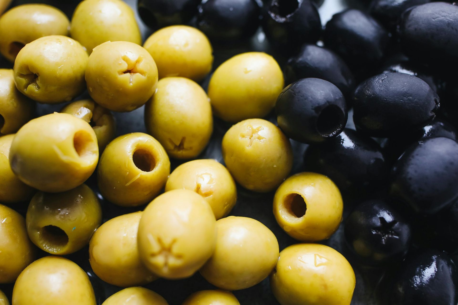 Montón de aceitunas amarillas y negras, algunas sin hueso, apiladas muy juntas.