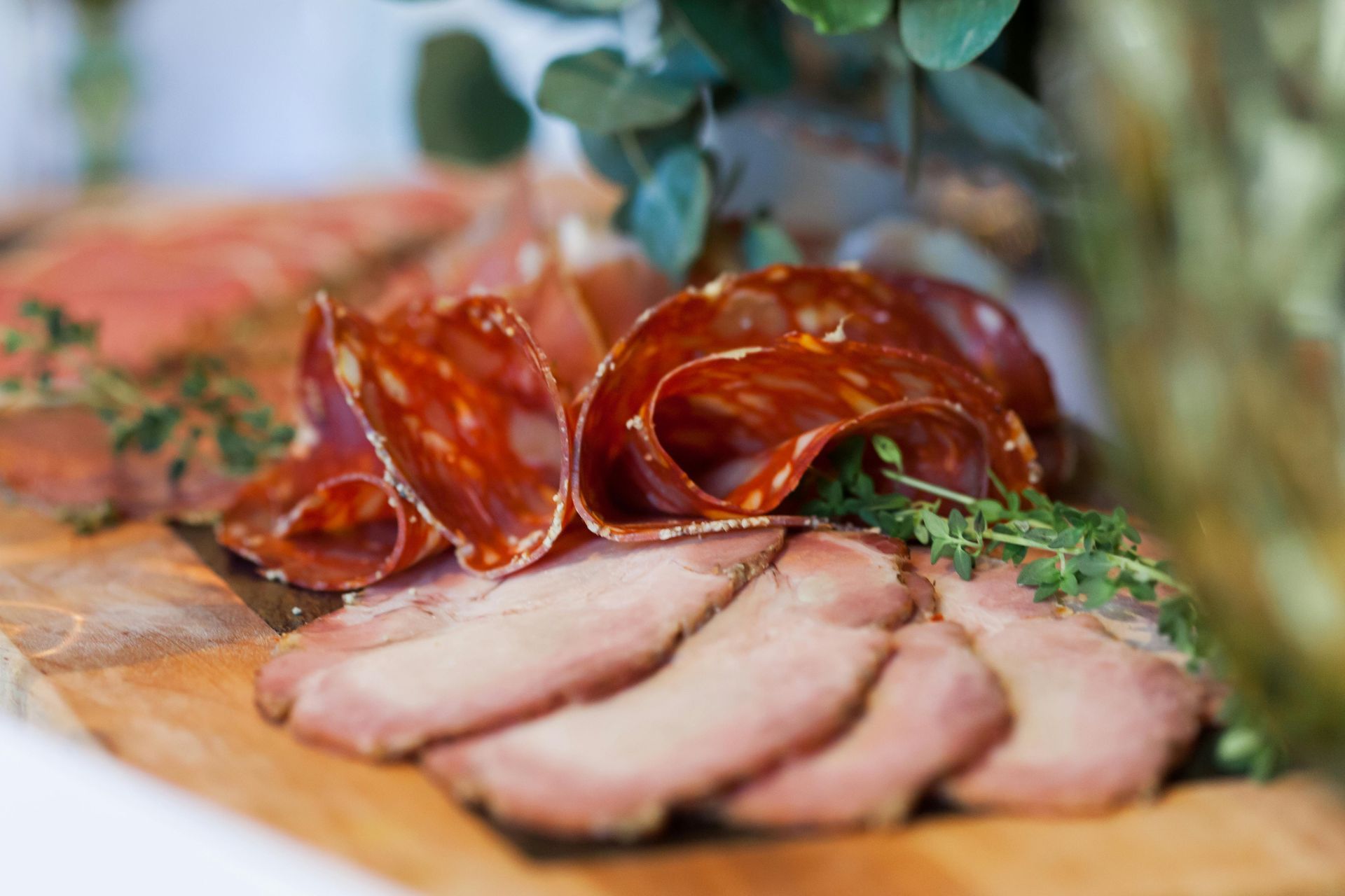 Lonchas de embutido curado y lonchas asadas dispuestas sobre una tabla de madera con hierbas aromáticas y verduras.