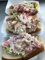 Three lobster rolls on paper, filled with lobster salad and lettuce.