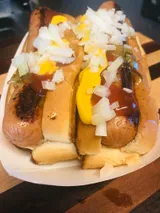 Two hot dogs in buns, topped with mustard, ketchup, and chopped onions, in a paper tray.