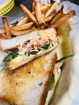 Sandwich with fries, cut in half. Toasted bread, filling with shredded ingredients and arugula, served with golden fries.