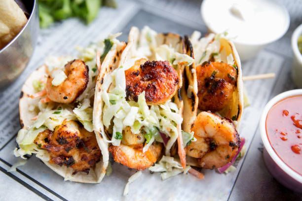 Grilled shrimp tacos with slaw, served with sauces.