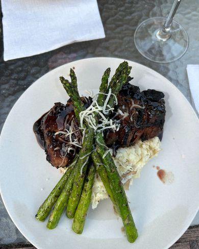 Lobster dinner on a white plate: lobster, corn on the cob, baked potato, roll, and side dishes.