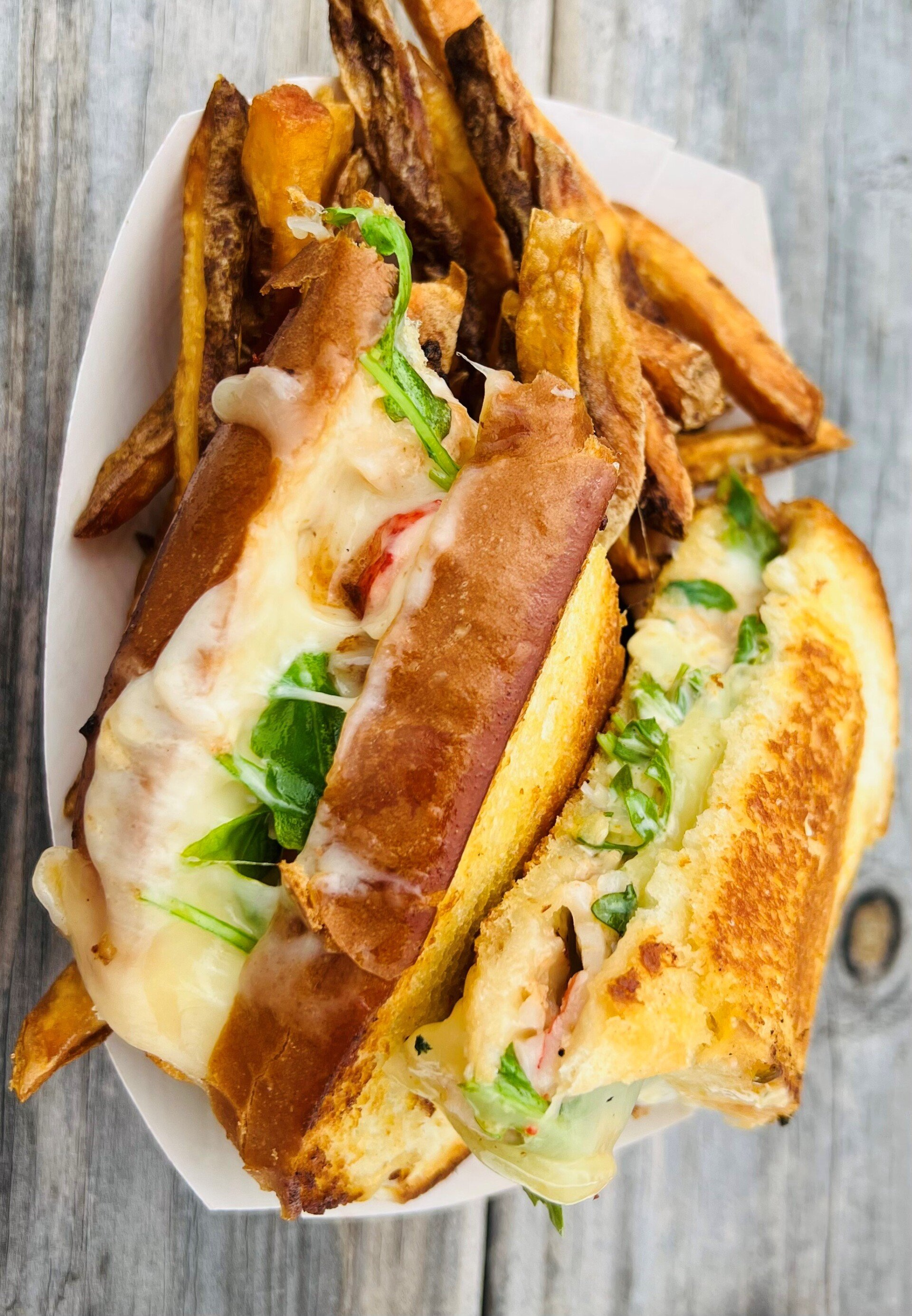 Grilled cheese sandwich with fries in a paper container on a wooden surface.