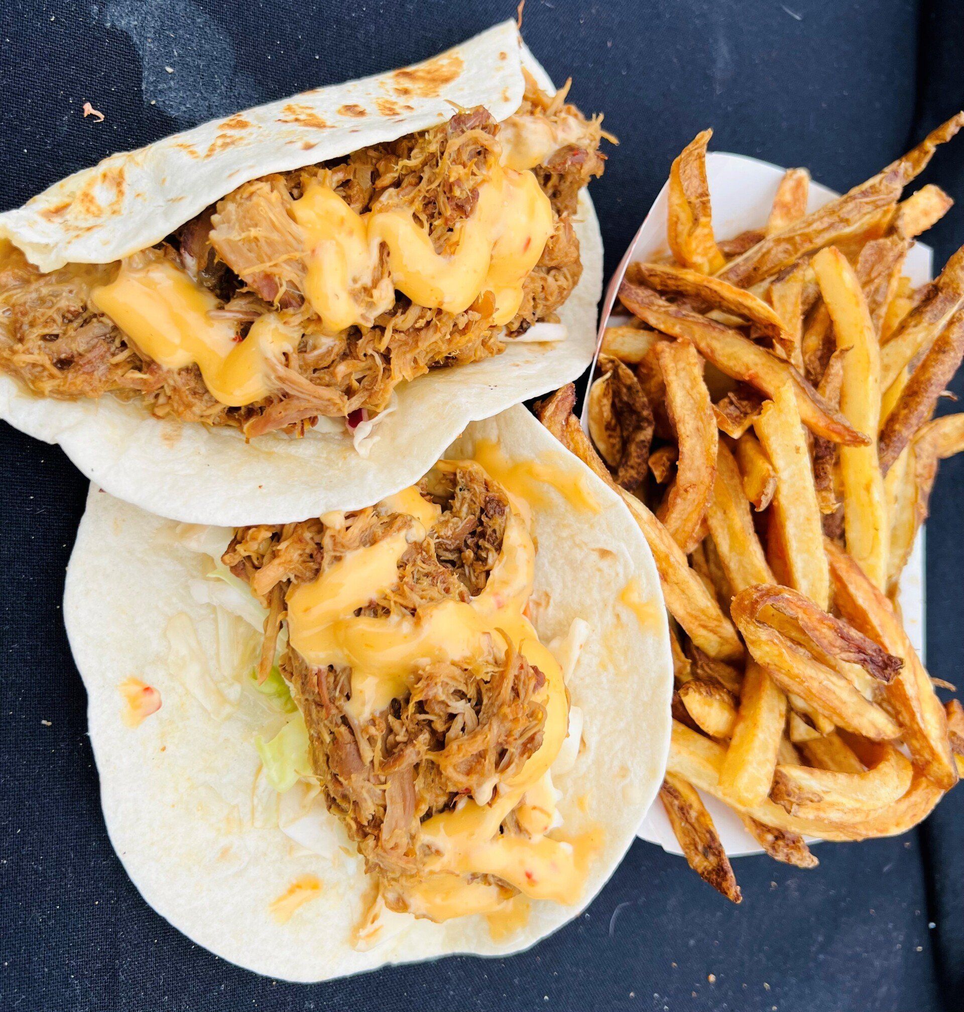 Two tacos with shredded meat and cheese, beside a container of fries.