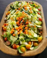 Salad in a wooden bowl: Lettuce, cucumbers, cherry tomatoes, and diced carrots.