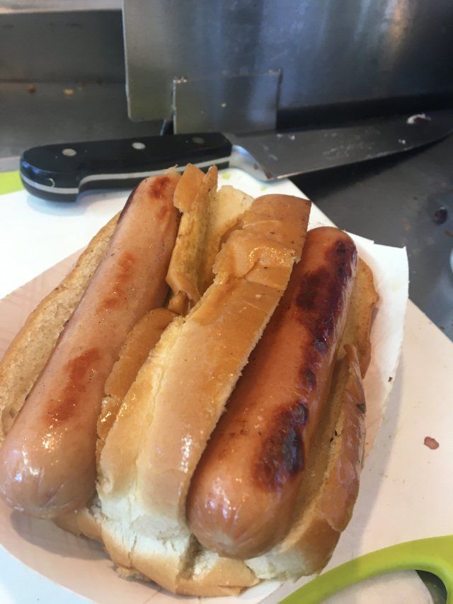 Two grilled hot dogs in a toasted bun, served on paper with a knife in the background.