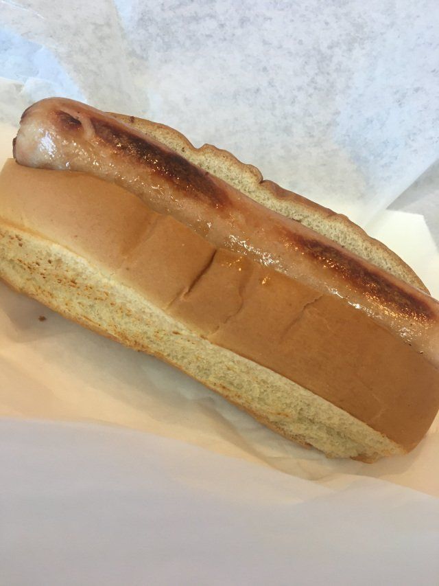 Hot dog in a bun, with a grilled top. Placed on white paper.