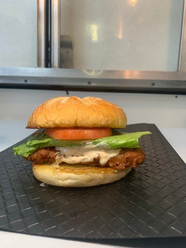 Fried chicken sandwich with lettuce, tomato, and sauce on a bun.