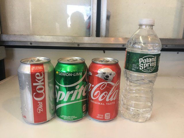 Four beverages: Diet Coke, Sprite, Coca-Cola, and a water bottle lined up on a surface.