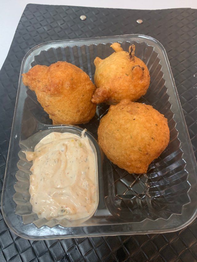Three golden-brown hushpuppies with a creamy dipping sauce in a clear plastic container.