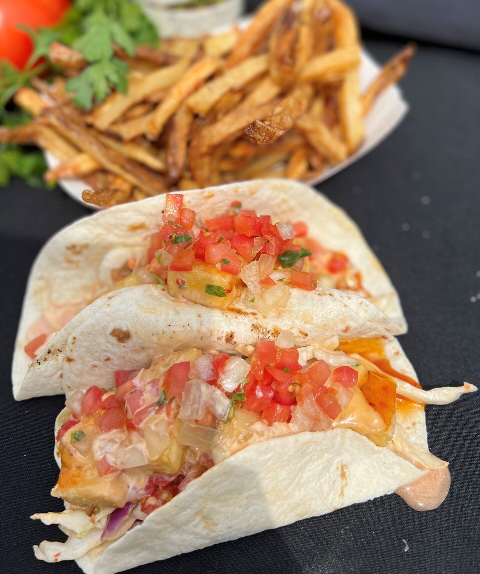 Two tacos with tomato salsa, fries in a container, tomato, and parsley.