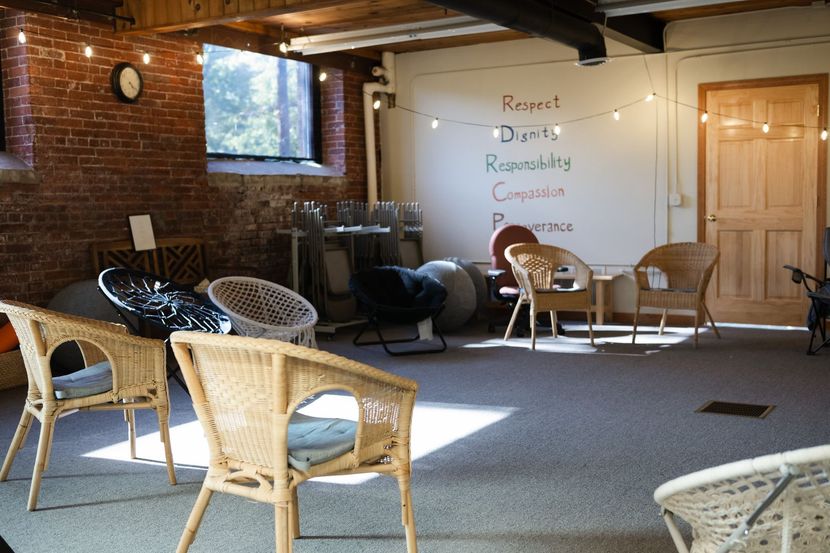 A room with a brick wall, chairs arranged in a circle, and a white wall with the words Respect, Dignity, and Compassion.