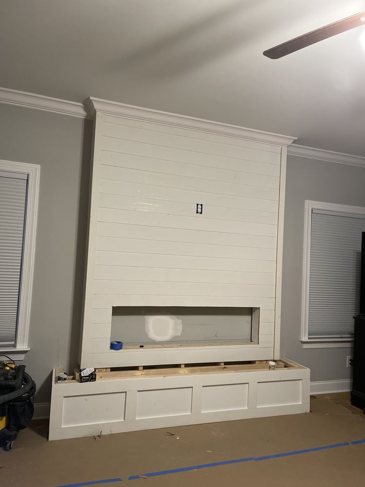 White paneled fireplace build with storage bench, gray walls, and crown molding.