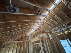 Wooden framing of a house under construction; exposed rafters, trusses, and wiring.