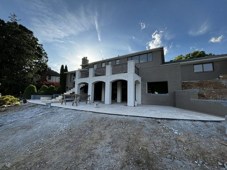 A gray stucco house under construction, white columns, a sunny blue sky, and gravel ground.