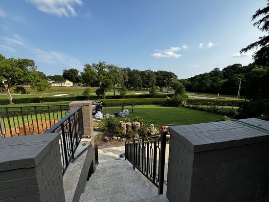 View from steps overlooking a golf course with green grass, trees, and a blue sky.