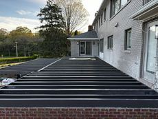 Black deck frame extending from a brick wall, attached to a two-story white brick building with windows.