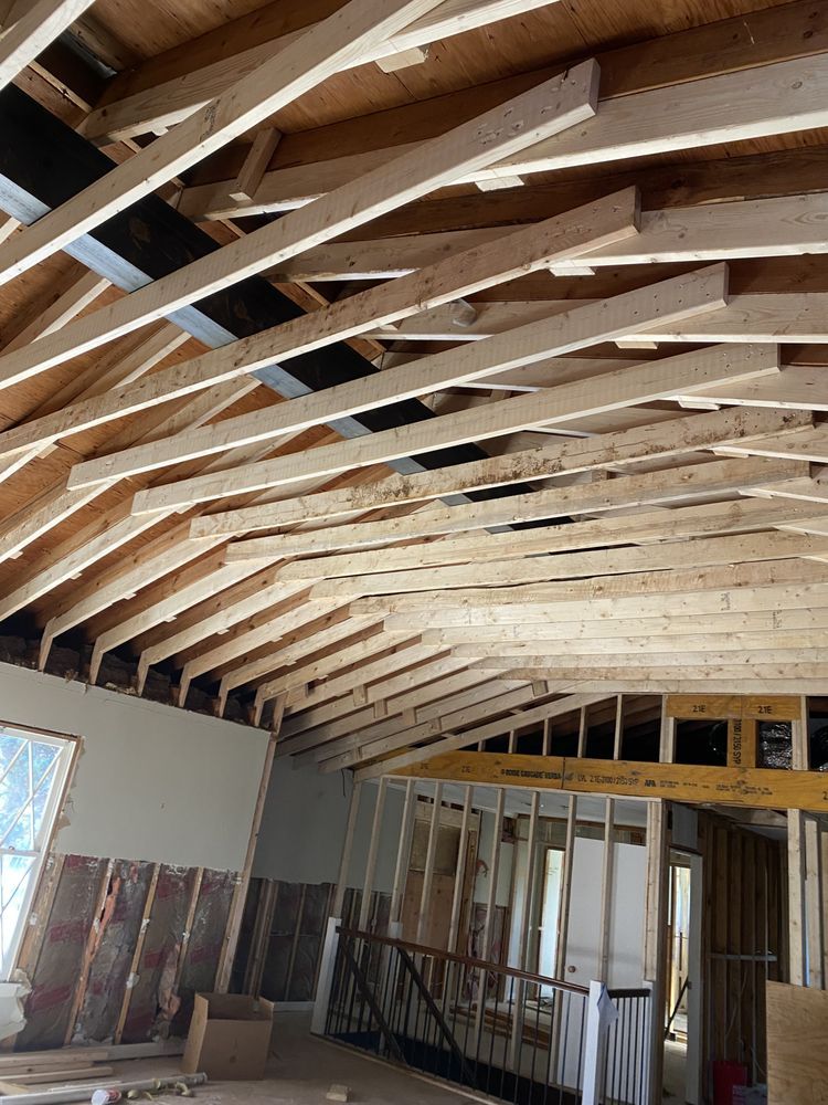 Interior view of a room under construction, showing exposed rafters, framing, and a partially built wall.