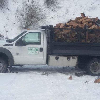 A white truck filled with logs is parked in the snow.
