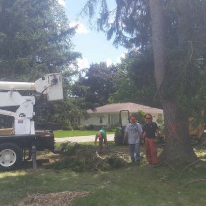 A couple of men standing next to a tree in front of a truck.
