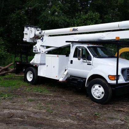 A white truck with a crane on top of it is parked in a dirt field.